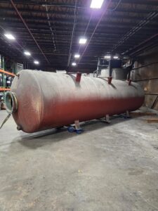 A large, cylindrical steel tank with welded support brackets rests on blue blocks inside an industrial warehouse during a tank removal project in Lynn.